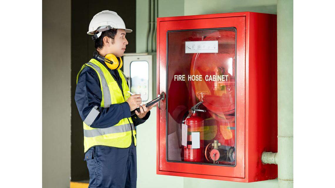 Building inspector man using digital tablet checking fire hose cabinet.