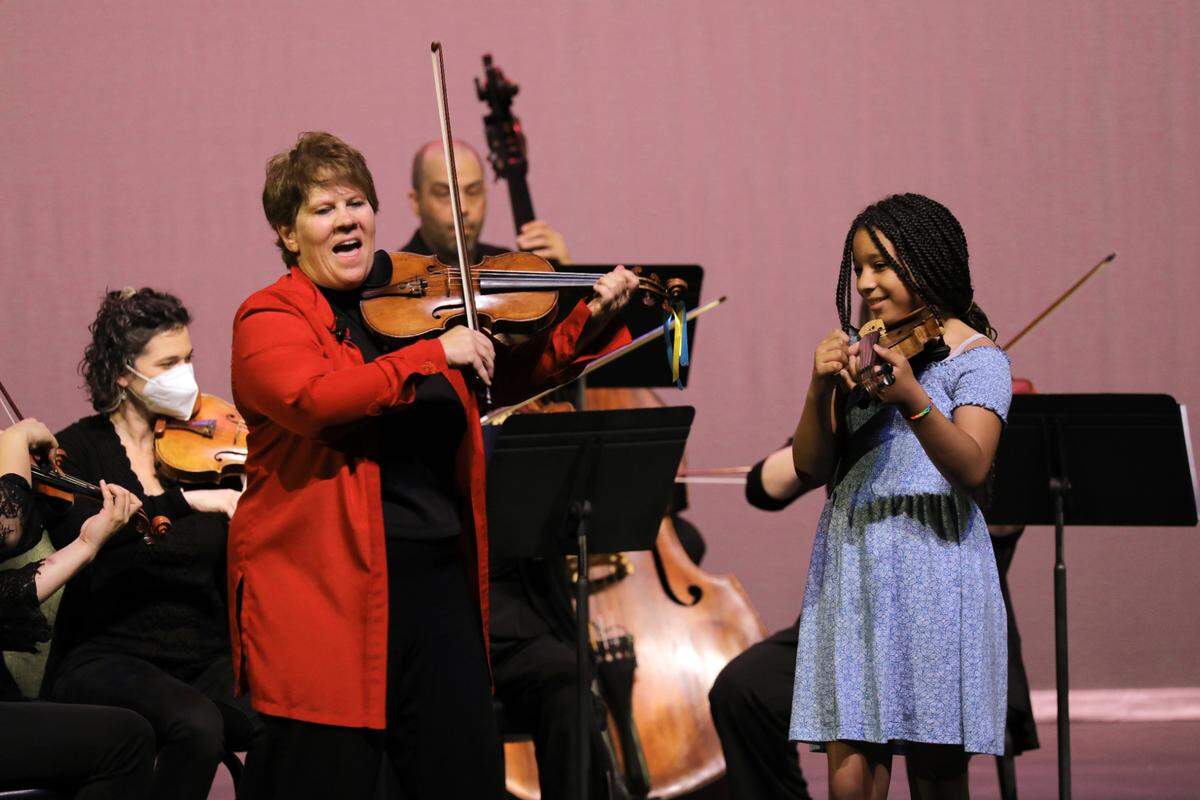 A student joins musician Dawn Harms and the Merced Symphony Orchestra on stage at the Merced Symphony Children’s Concert at the Merced Theatre on April 7, 2022.