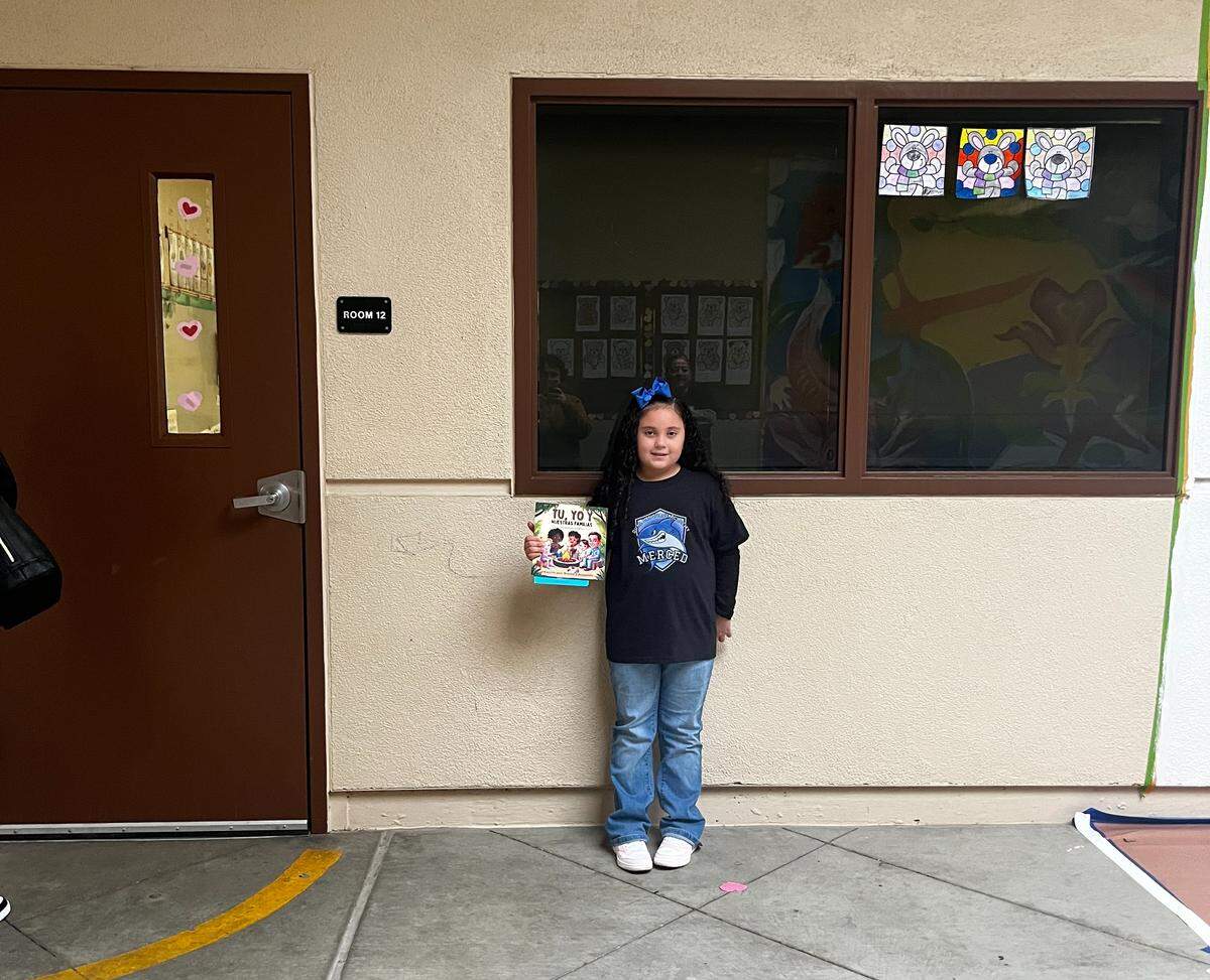 First-grade student Aliviya stands outside her classroom at the Dual Language Academy. She is wearing a graphic t-shirt with a shark on it.