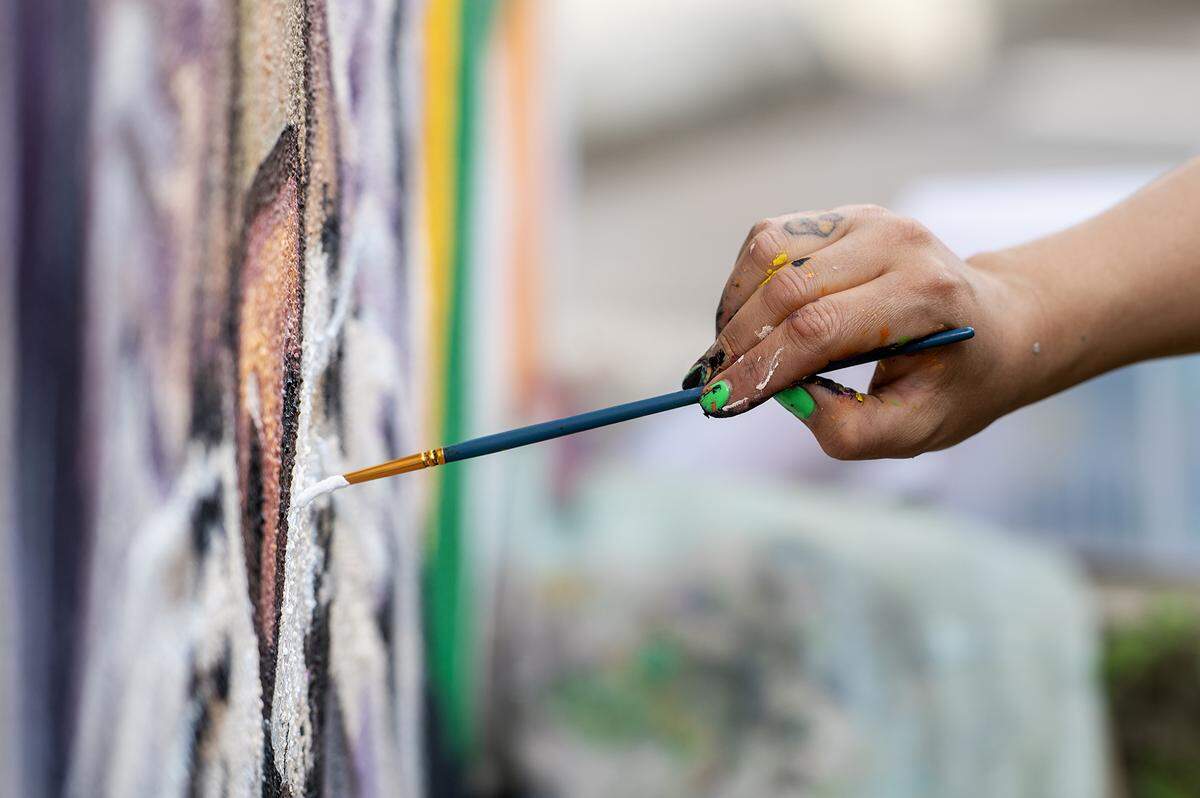 Fresno artist Andrea Torres, 35, paints a mural on the walls of a dumpster enclosure in a parking lot off of West 18th Street in Merced, Calif., on Feb. 27, 2025. Torres said her mural is meant to represent community pride while including elements of the natural valley landscape and touching on the connection the city has with nearby UC Merced.