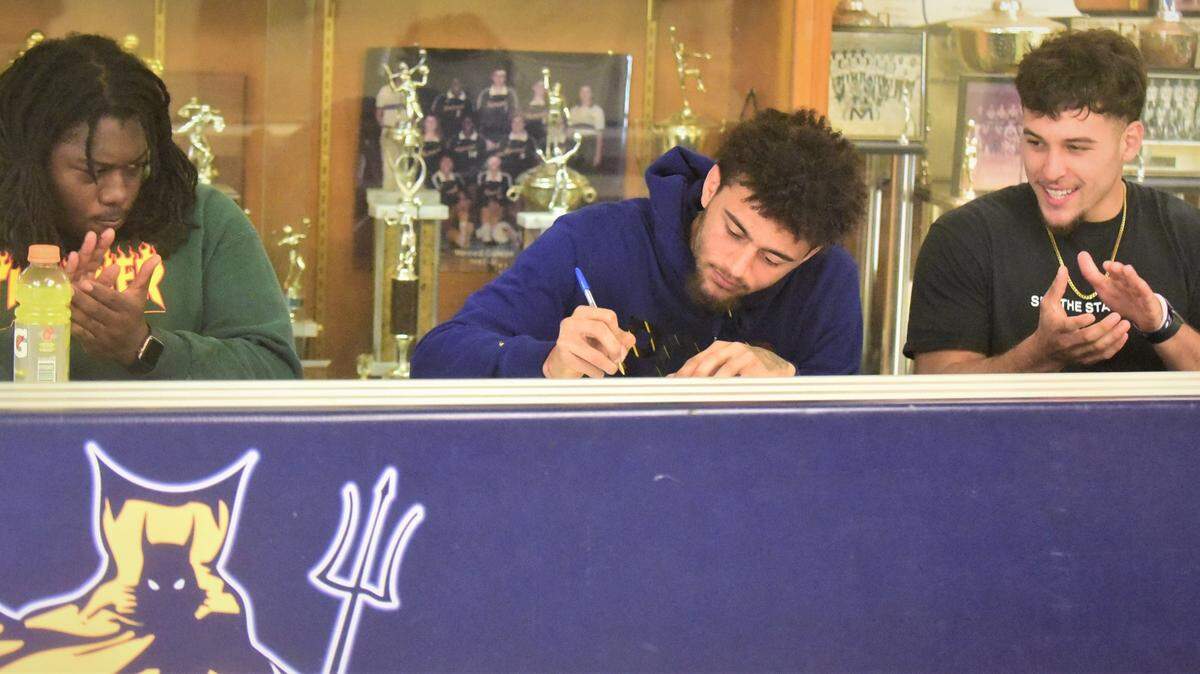 Merced College receiver Desani Tate signs his national letter of intent to accept a football scholarship to McPherson College in Kansas while teammates Azyia Vance (left) and Nate Ruiz look on during a signing ceremony at Merced College on Monday, April 4, 2022.