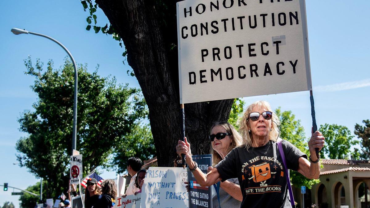 A woman who identified herself as Jennifer, holds a sign as she and other protesters take part in a “No Kings” protest in Merced,