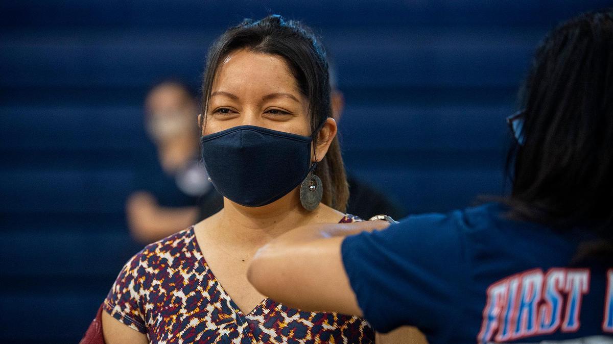 Norma Chavez, a Merced County Office of Education college and career advisor for migrant education, receives a COVID-19 vaccine at a clinic inside the Cesar E. Chavez Middle School gymnasium in Planada, Calif., on Thursday, March 4, 2021.