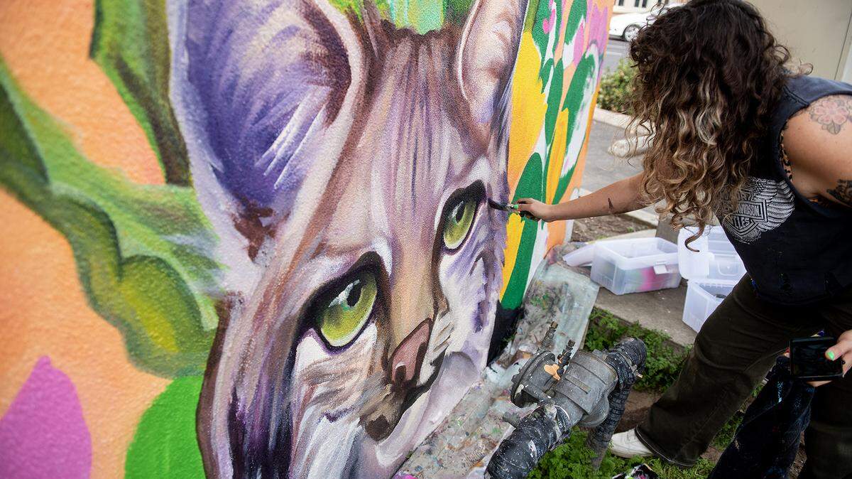 Artist Andrea Torres, 35, of Fresno, paints a mural on the walls of a dumpster enclosure in a parking lot off of West 18th Street in Merced, Calif., on Feb. 27, 2025. Torres said her mural is meant to represent community pride while including elements of the natural valley landscape and touching on the connection the city has with nearby UC Merced.