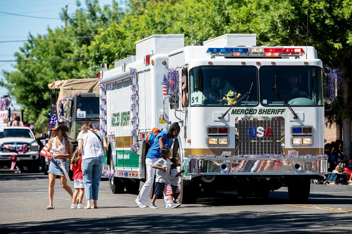 Children run to receive stickers from the Merced County Sheriff’s Office during a Fourth of July parade in Atwater, Calif., on Monday, July 4, 2022.