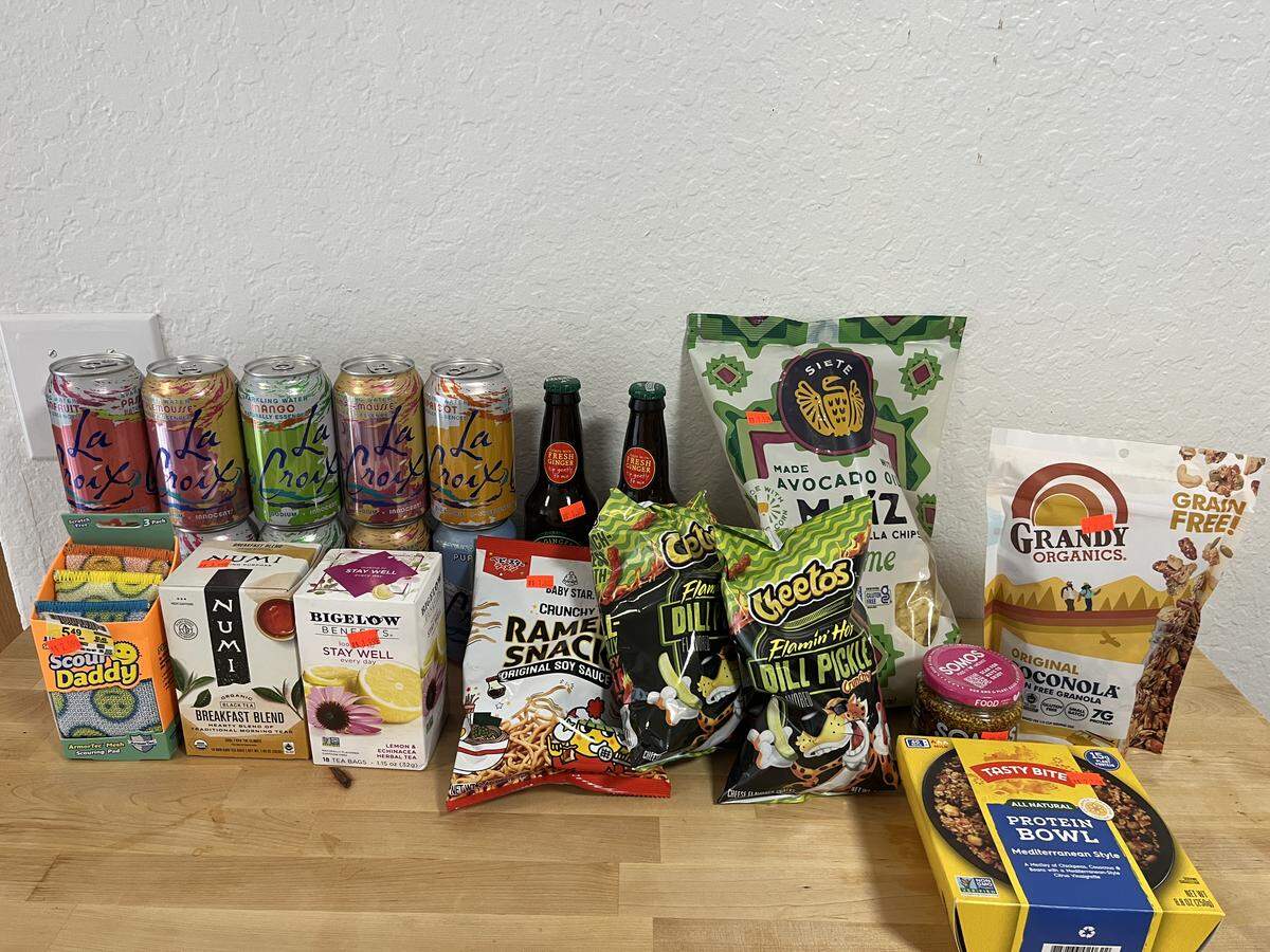 All the snacks, drinks, and items I purchased are laid out on a wooden table.