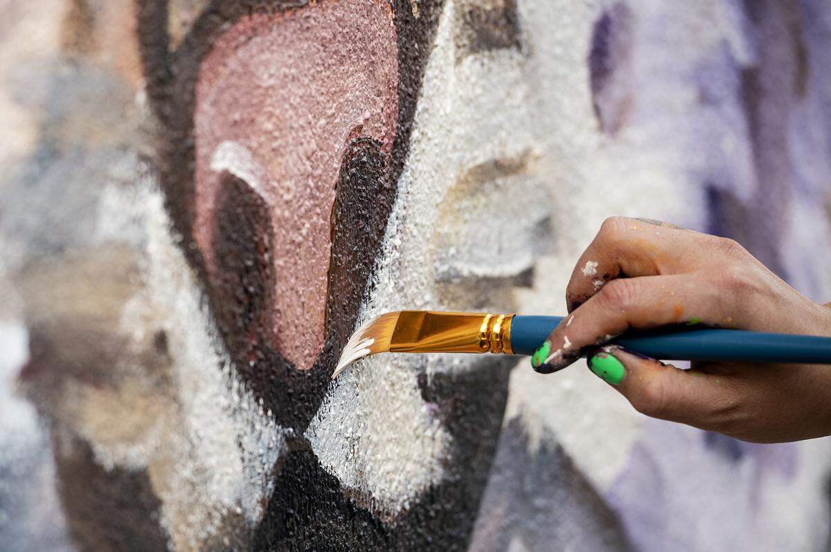 Fresno artist Andrea Torres, 35, paints a mural on the walls of a dumpster enclosure in a parking lot off of West 18th Street in Merced, Calif., on Feb. 27, 2025. Torres said her mural is meant to represent community pride while including elements of the natural valley landscape and touching on the connection the city has with nearby UC Merced.