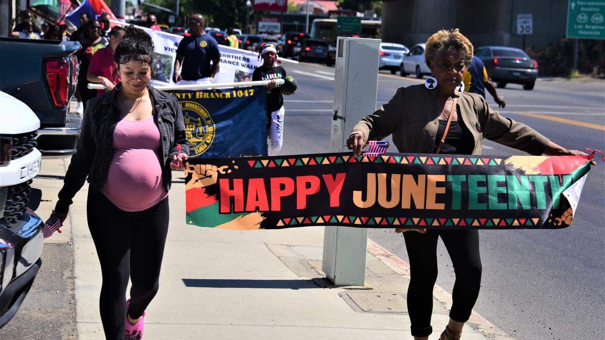 Alyssha Pierce and Diana Pierce display a Happy Juneteenth banner as they march down Martin Luther King Jr. Way during the first Juneteenth Parade in Merced, Calif. on Saturday, June 18, 2022.