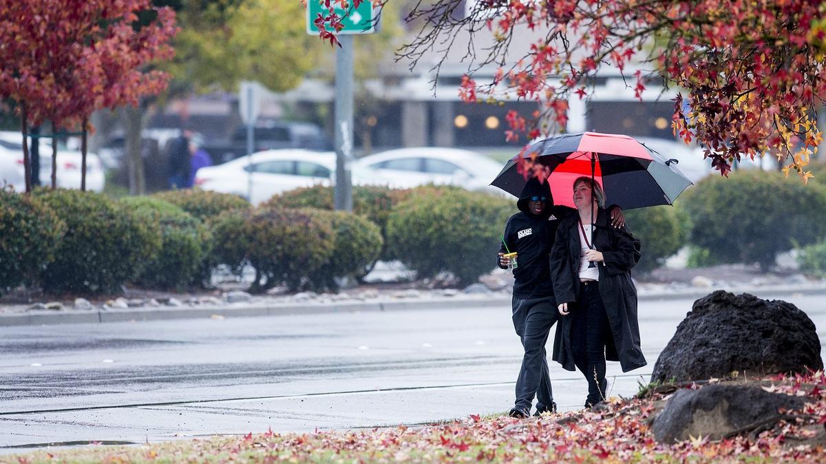 Pedestrians walk along G Street as rain showers move through Merced, Calif., on Friday, Nov. 23, 2018.