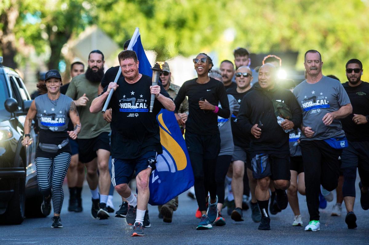 Merced resident and Special Olympics athlete Mark Heffner, 42, carries the torch containing the “Flame of Hope” along West Main Street during the annual Law Enforcement Torch Run for Special Olympics Northern California in Merced, Calif., on Wednesday, June 26, 2024. Heffner is a multi-sport athlete who competes in basketball, TOPSoccer, track and field and golf.