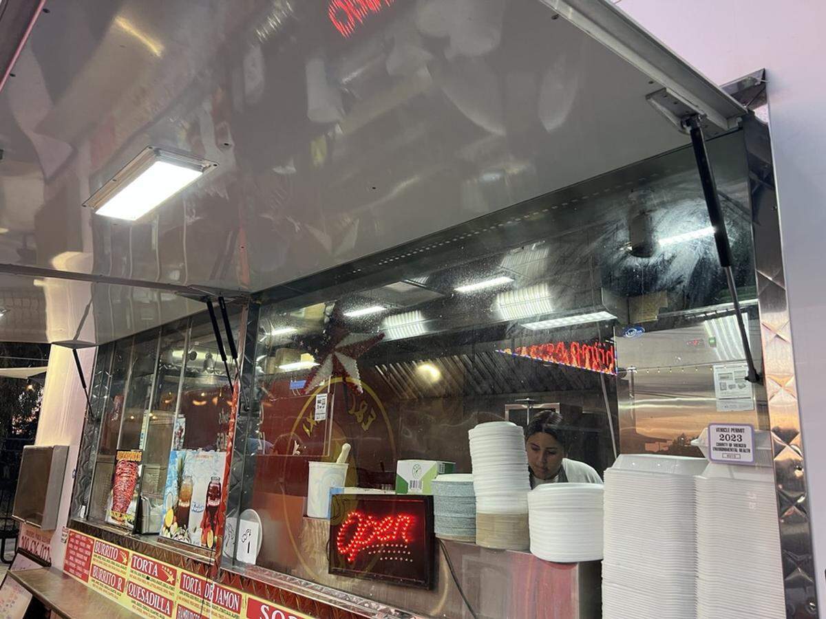 A woman cooks seen through the window of a food truck.