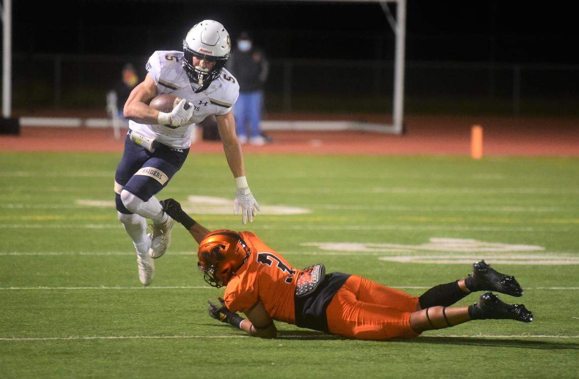 Central Catholic running back Jack Grisel (5) jumps to avoid the tackle of Merced safety Quincy Collins during a game on Thursday, March 25, 2021 at Veterans Stadium in Merced, Calif.