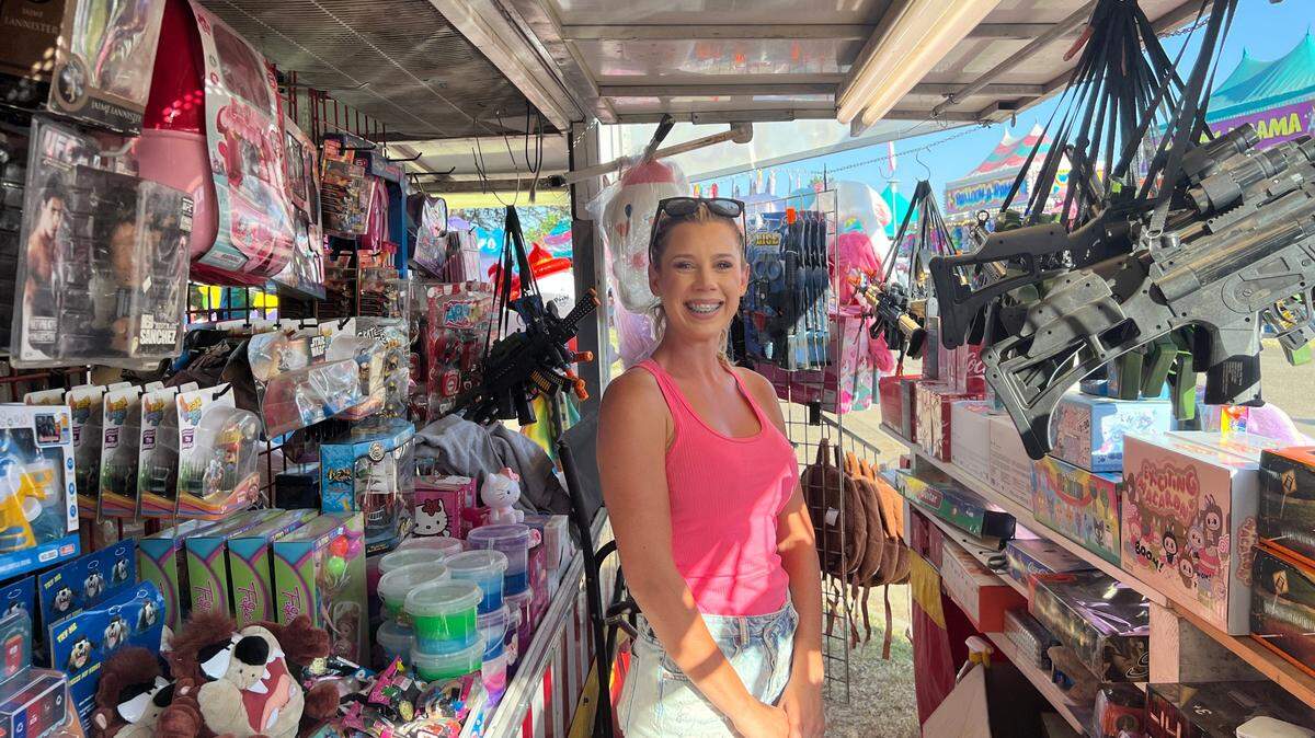A woman stands outdoors with stacks of toys on either side of her.
