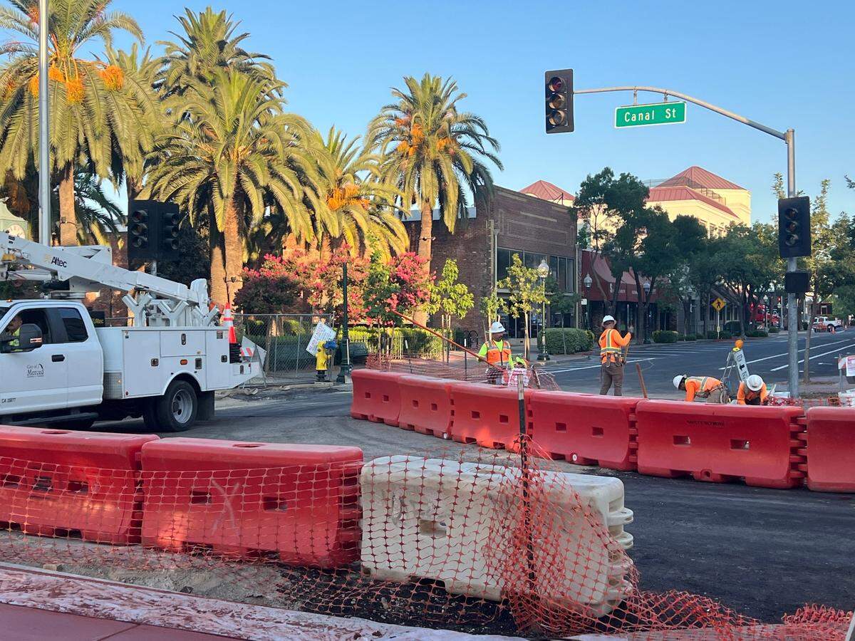 A group of men in orange shirts and vest work on Canal Street behind plastic barriers directing traffic.