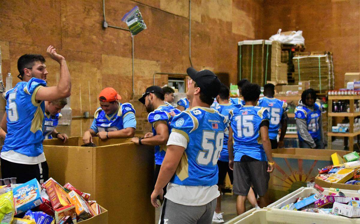 Former Buhach Colony football player Brendan Ekizian (5)tosses a bag of food to be sorted to Mason Reel (58) at the Merced County Food Bank on Tuesday, June 18, 2019.