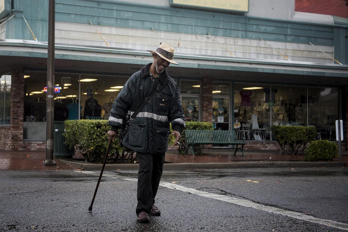 Vincent T. Madden, 59, crosses West Main Street as rain showers move through Merced, Calif., on Friday, Nov. 23, 2018.