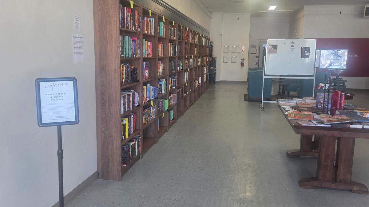 A bookstore interior with bookshelves along the left wall and tables covered in books in the center