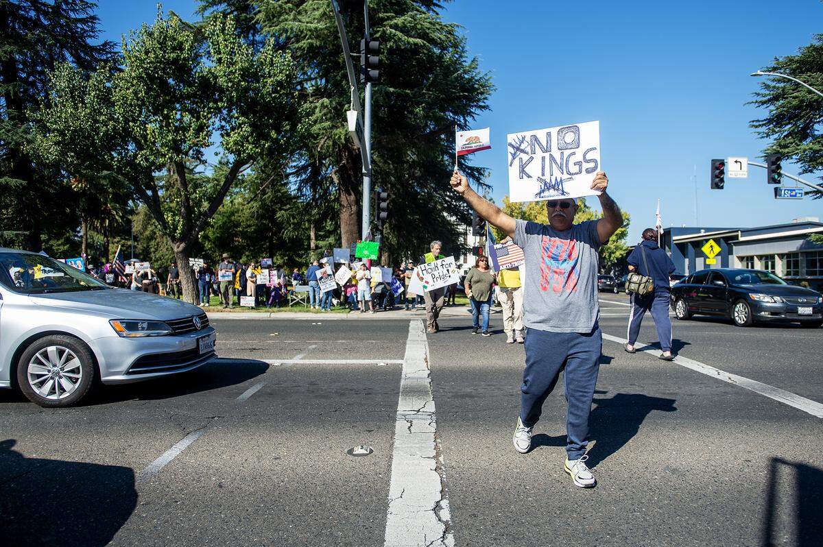 Protesters carry signs while crossing M Street during a “No Kings” protest in Merced, Calif., on Saturday, Oct. 18, 2025.