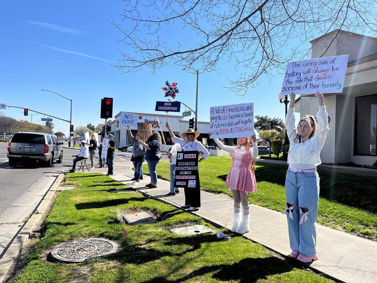 Protestors hold signs at the intersection of M Street and Olive Avenue.