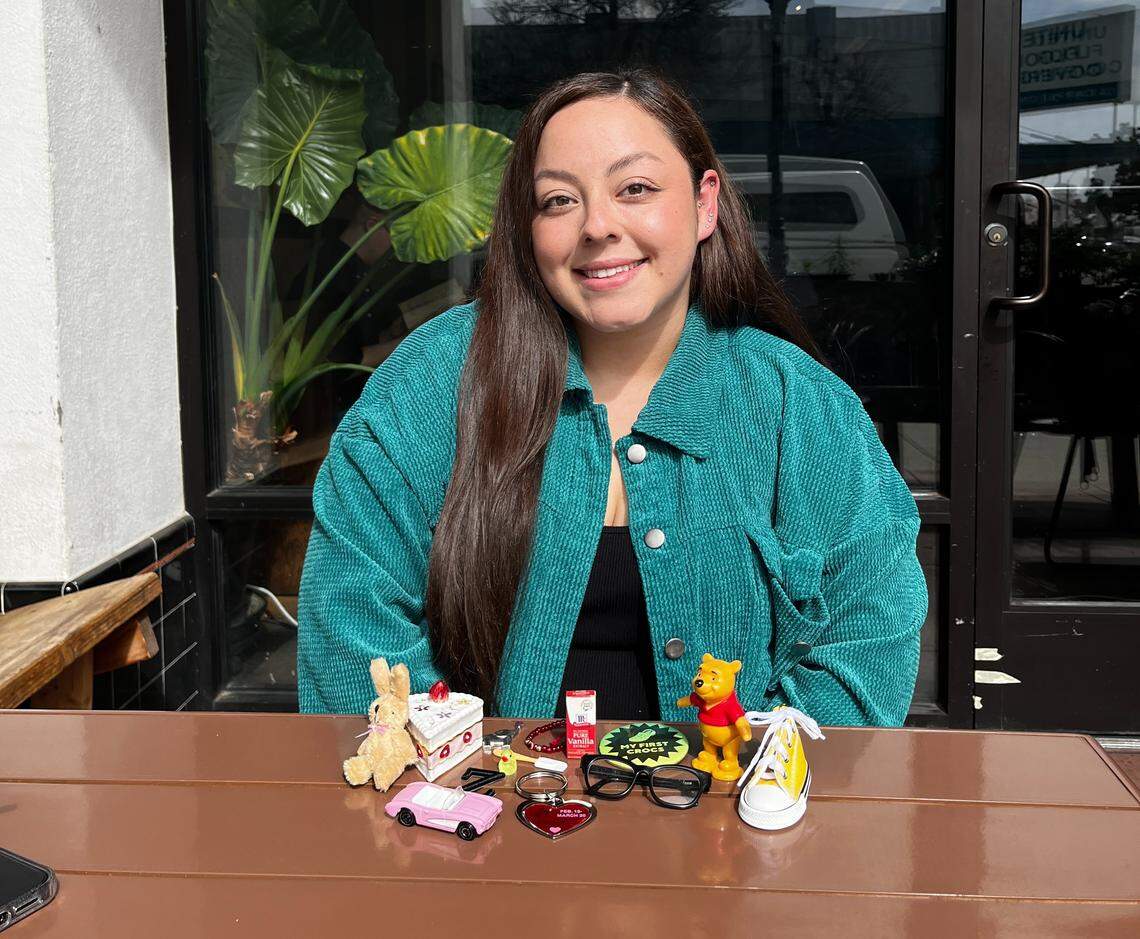 Liz Jarquin sits at a cafe table with an assortment of small figurines in front of her.