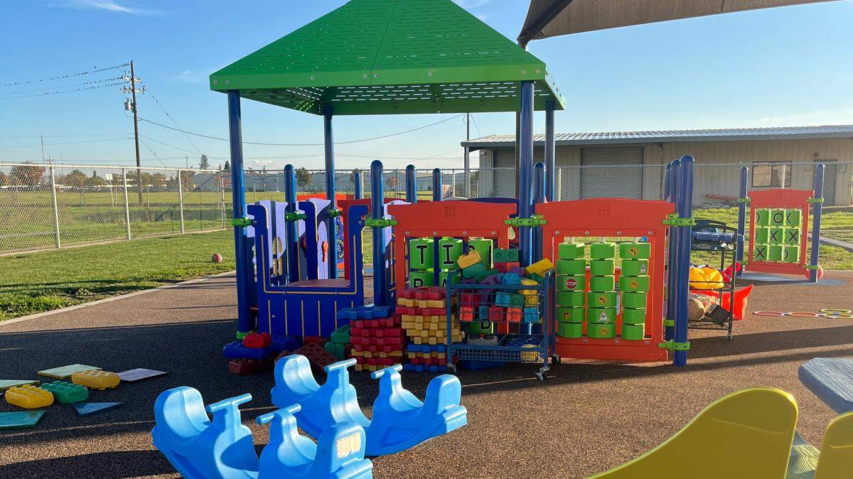 An outdoor play structure for preschool age children with toys scattered on the ground.