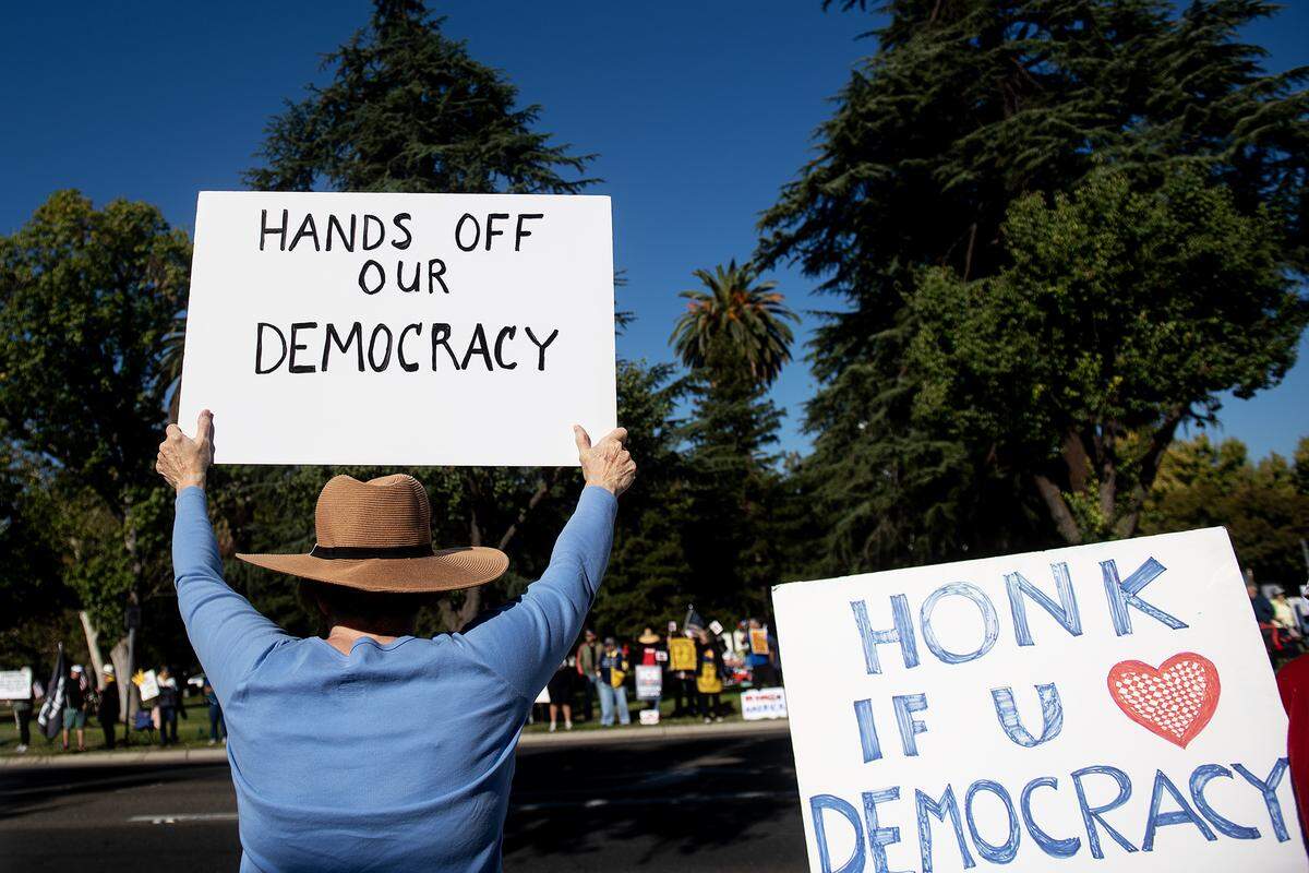 Protesters hold signs along M Street during a “No Kings” protest in Merced, Calif., on Saturday, Oct. 18, 2025. 