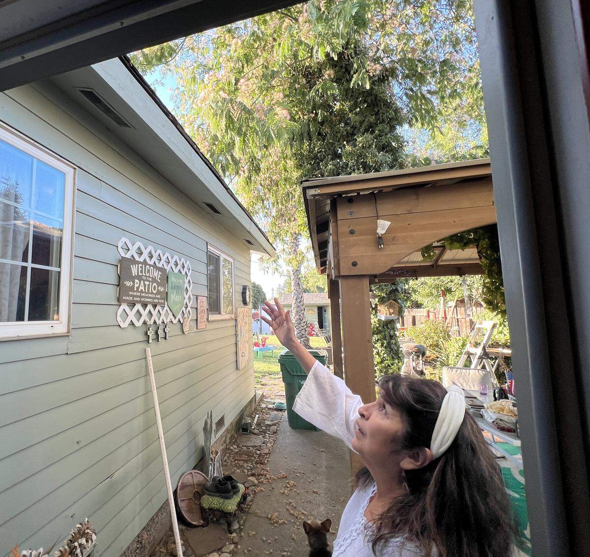 A woman points upward to the roofline while standing on a patio.