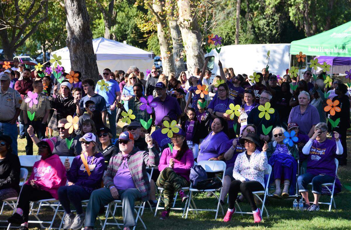 The crowd holds up different color flowers during a ceremony prior to the Walk to End Alzheimer’s at Applegate Park on Saturday, Oct. 5, 2019 in Merced, Calif.