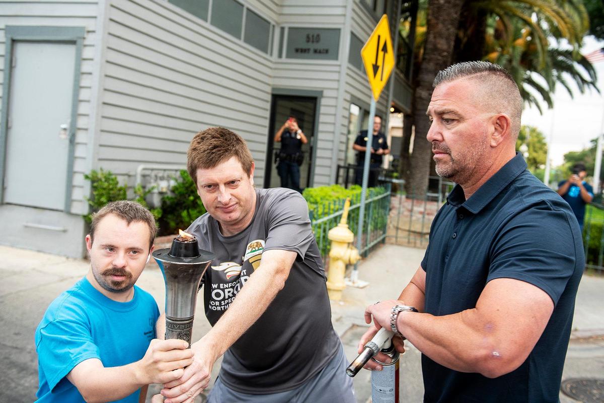 Athletes Dallas Young, 26, left, and Mark Heffner, 40, center, both of Merced, hold the Special Olympics Torch as Ceres police officer and Special Olympics Northern California board member Jeff Godfrey, right, lights the “Flam of Hope” during the Law Enforcement Torch Run for Special Olympics Northern California in Merced, Calif., on Wednesday, June 22, 2022. This year marks the 25th anniversary of the Law Enforcement Torch Run for the Special Olympics Northern California.