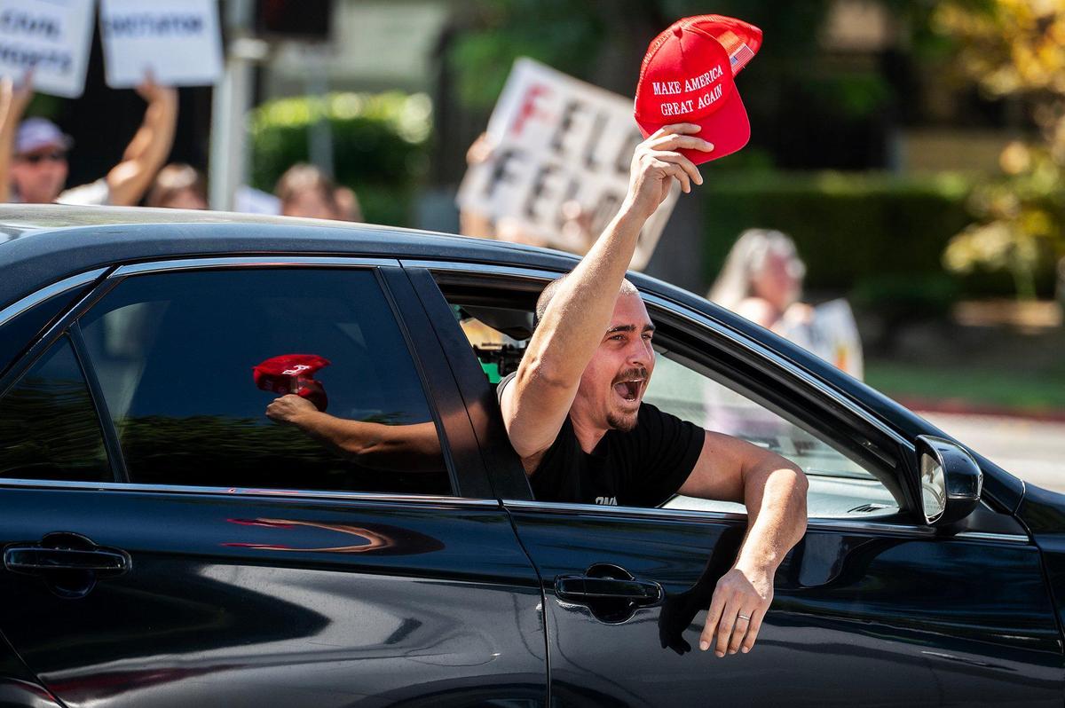 A man waving a “Make America Great Again” hat leans out the passenger side widow of a vehicle while yelling at those taking part in a “No Kings” protest along M Street in Merced, Calif., on Saturday, June 14, 2025.
