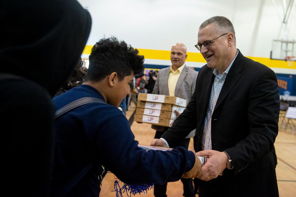 Comcast Chief Network Officer Elad Nafshi, right, hands out computers to eighth-graders during a ceremony announcing a $4.5 million investment to bring high-speed internet and broadband services to the area, at Cesar E. Chavez Middle School in Planada, Calif., on Monday, April 17, 2023. According to Nathan Ahle, Comcast Director of Government Affairs for the South Valley, the $4.5 million investment involves extending the existing network from nearby Merced into the town of Planada.