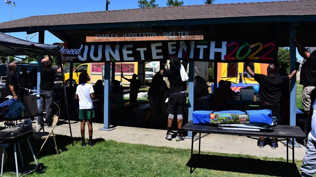 A group of men hang a banner with the words Juneteenth 2022