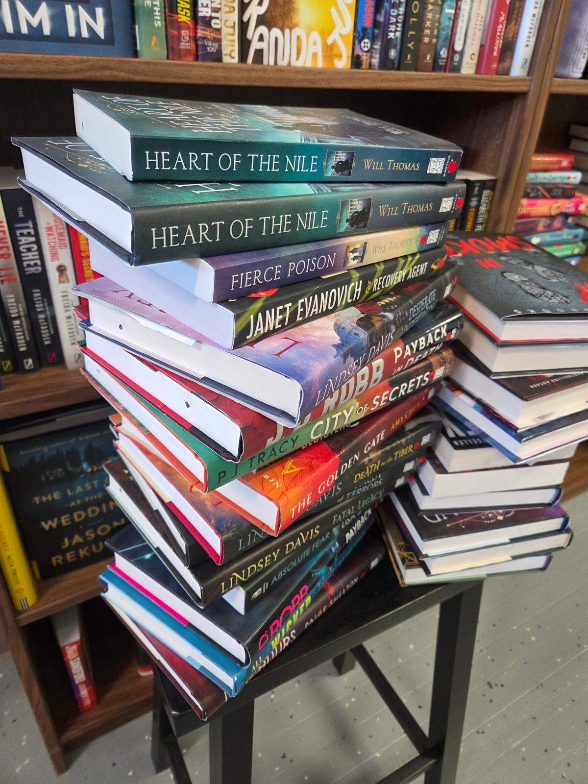 A stack of books on a stool in front of a bookshelf