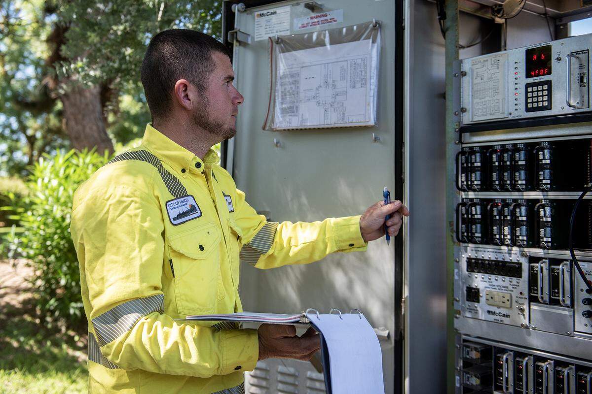 Tanner Harkreader, 28, a lead lighting technician with the City of Merced, performs routine maintenance on a traffic signal cabinet at the intersection of Olive and Parsons avenues in Merced, Calif., on Thursday, July 31, 2025. 