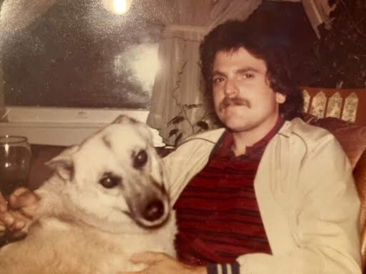 Stanley Howard is sitting with a large dog in his lap. He is holding a glass and looking directly into the camera.