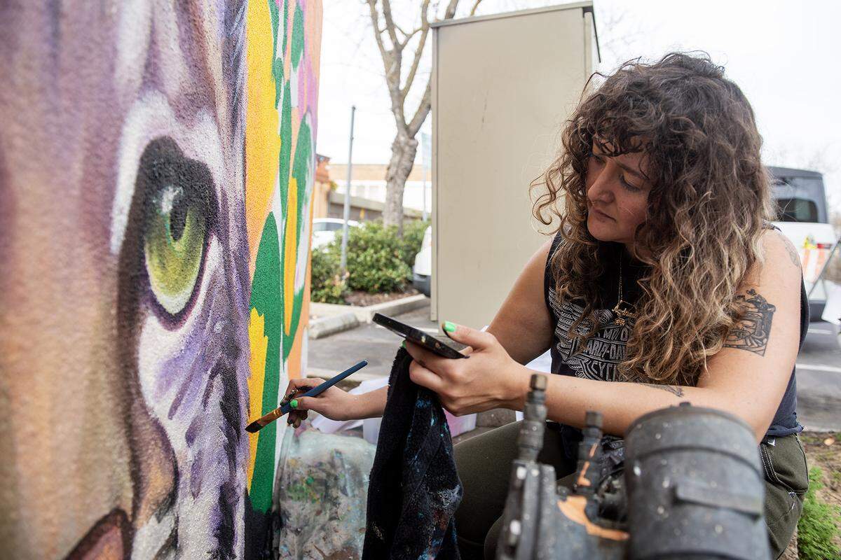 Artist Andrea Torres, 35, of Fresno, paints a mural on the walls of a dumpster enclosure in a parking lot off of West 18th Street in Merced, Calif., on Feb. 27, 2025. Torres said her mural is meant to represent community pride while including elements of the natural valley landscape and touching on the connection the city has with nearby UC Merced.