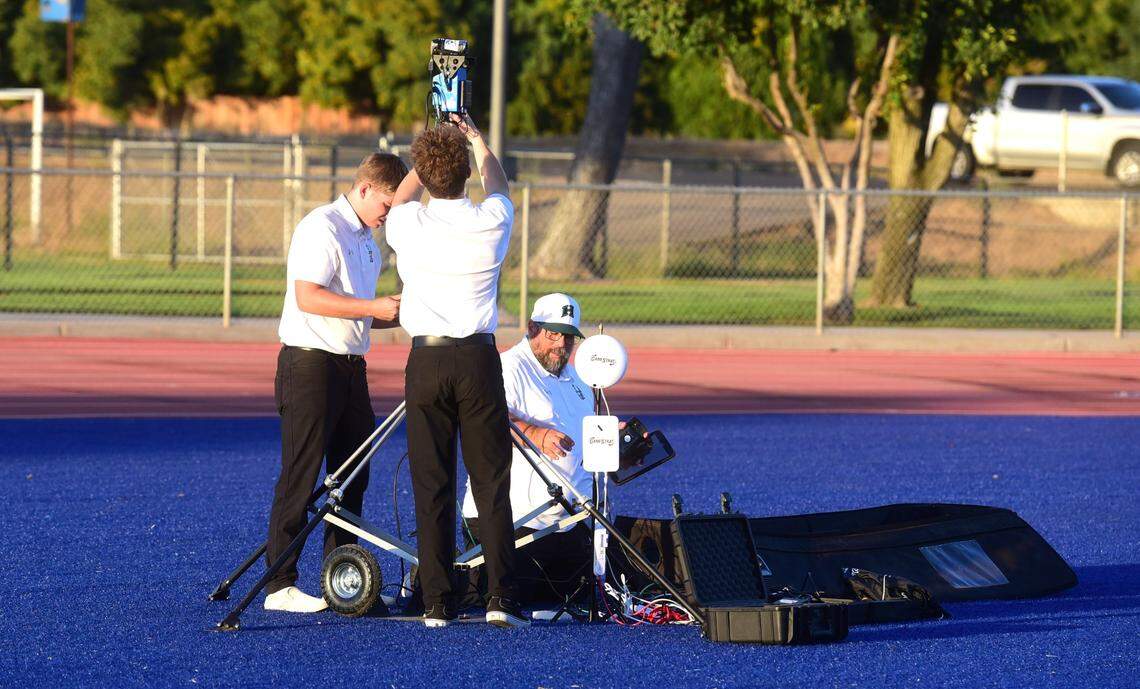 Hilmar High assistant coach Adam Komo (right) helps student volunteers set up their in-game video system GameStrat gear prior to a football game against Atwater High on Sept. 13, 2024 at Dave Honey Stadium.
