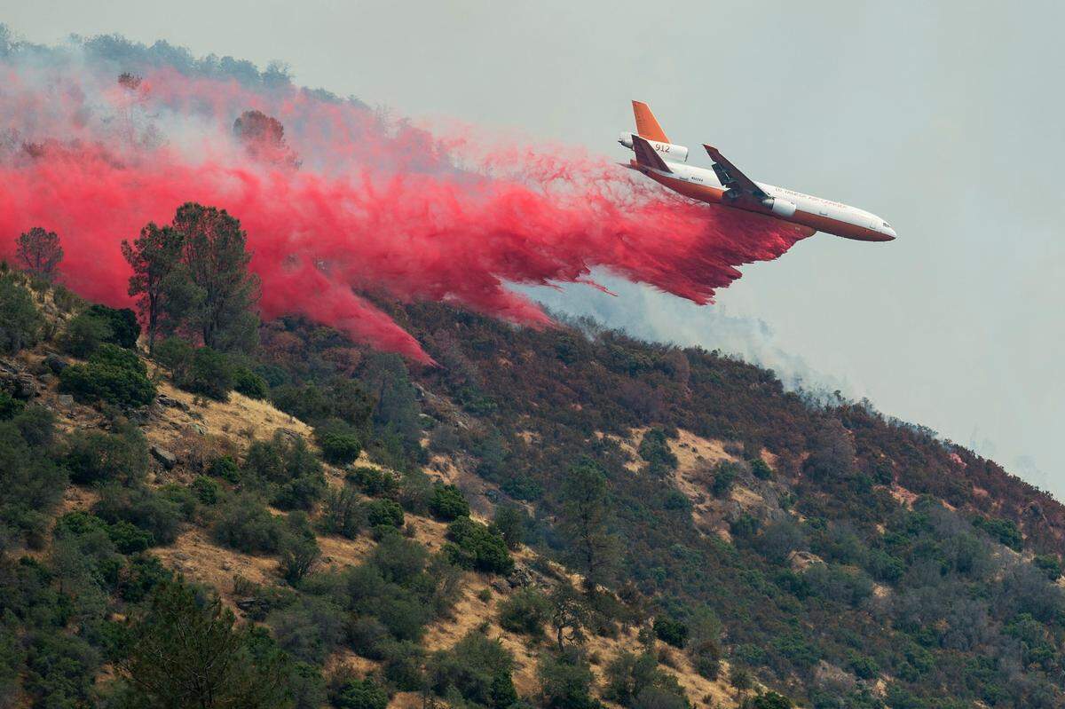 An airplane drops fire retardant onto a hilltop next to Lake McClure as fire crews continue to battle the Detwiler fire near Coulterville, Calif., on Thursday, July 20, 2017.