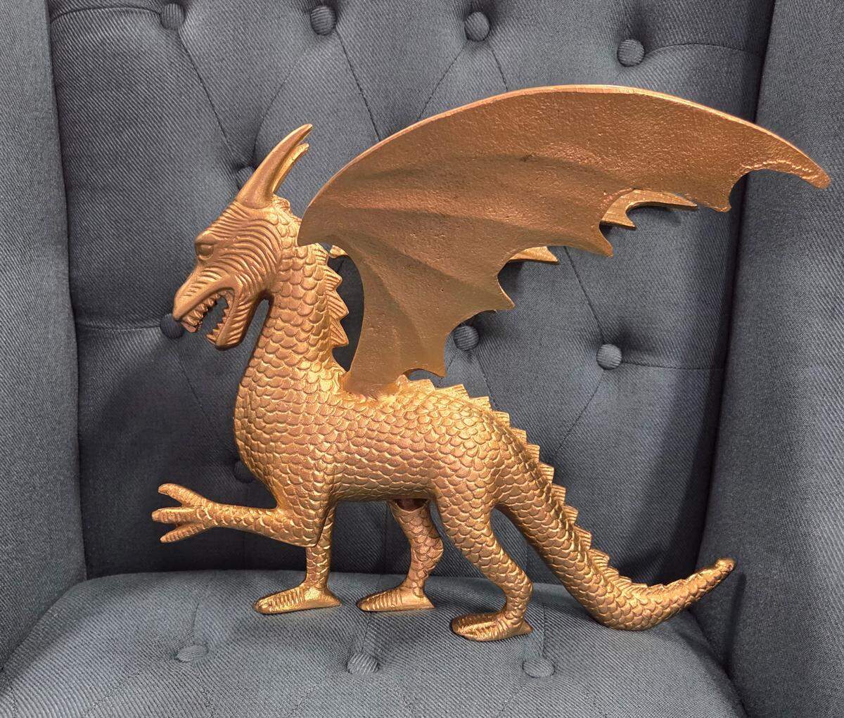 A golden dragon statue sits on a grey armchair.