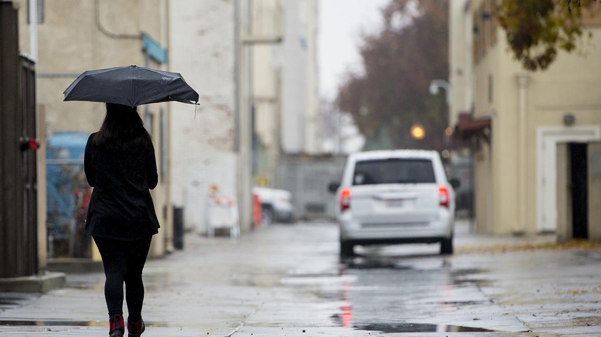 A woman uses and umbrella while walking down an alleyway as rain showers move through Merced, Calif., on Wednesday, Nov. 28, 2018.