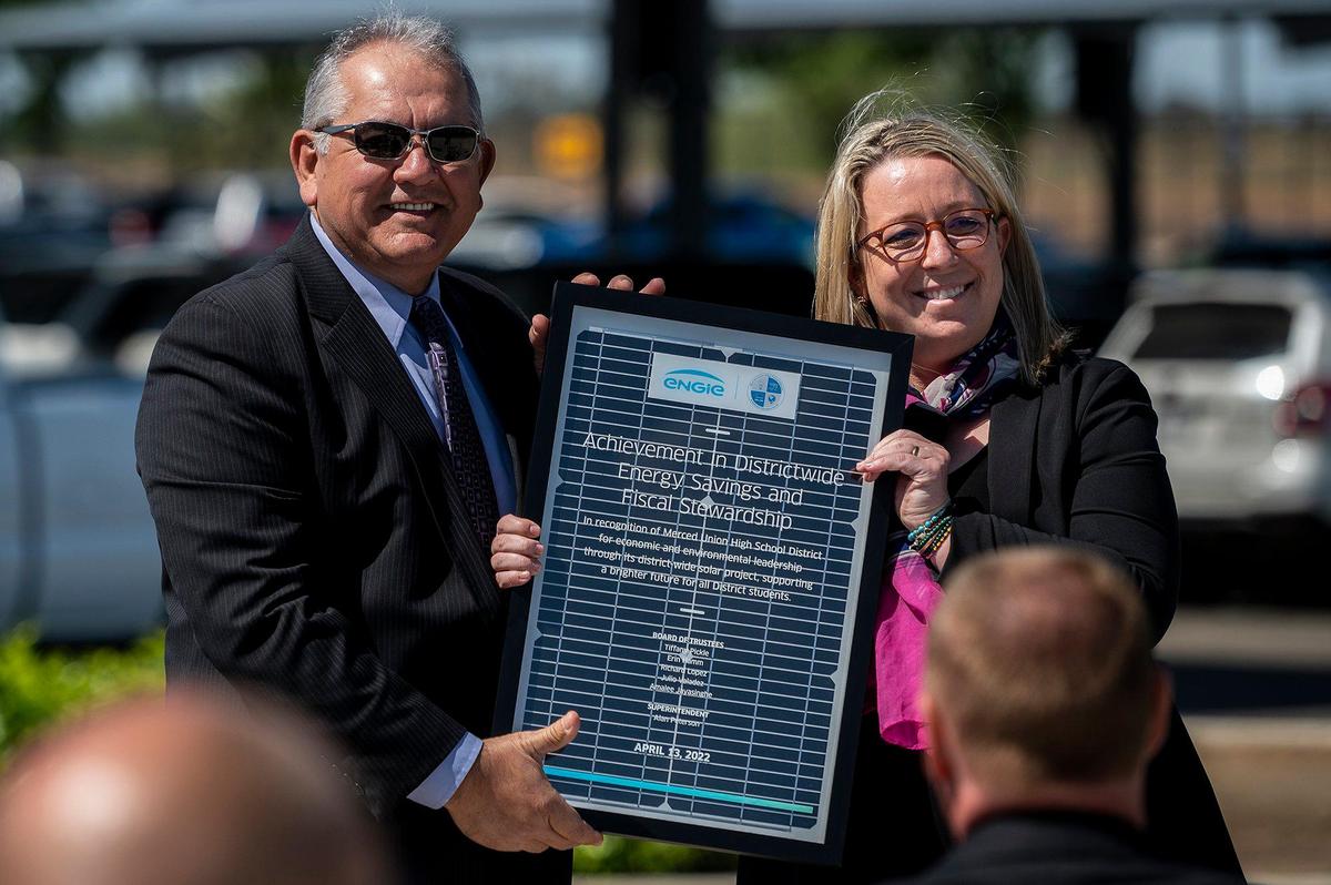 Courtney Jenkins, vice president of ENGIE Services, right, presents a plaque to Merced Union High School District Deputy Superintendent Ralph Calderon, left, during a ceremony celebrating the district’s renewable energy project at El Capitan High School in Merced, Calif., on Wednesday, April 13, 2022. Solar array structures have been installed at all Merced Union High School District parking lots and the panels are expected to supply the district with about 90% of its energy needs.