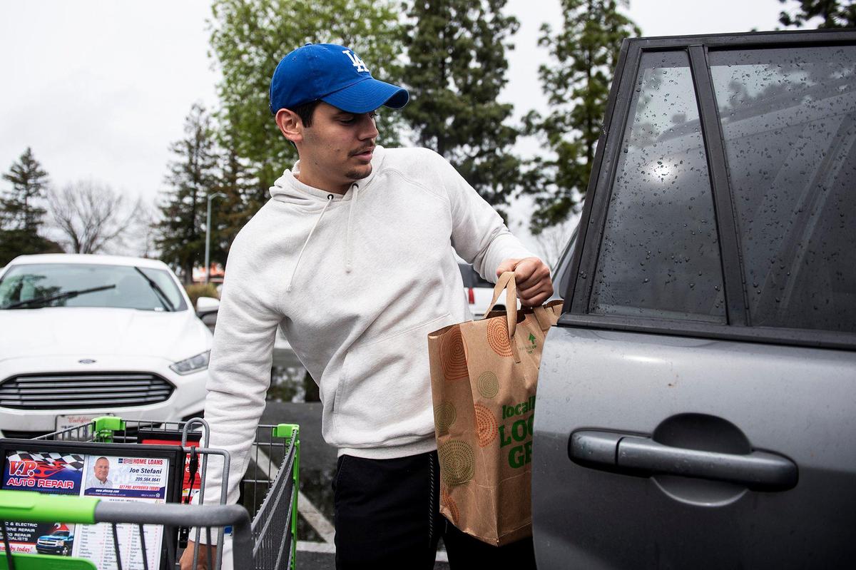 Adam Campos, 26, of Merced places groceries in a car after shopping at Save Mart in Merced, Calif., on Sunday, March 15, 2020.