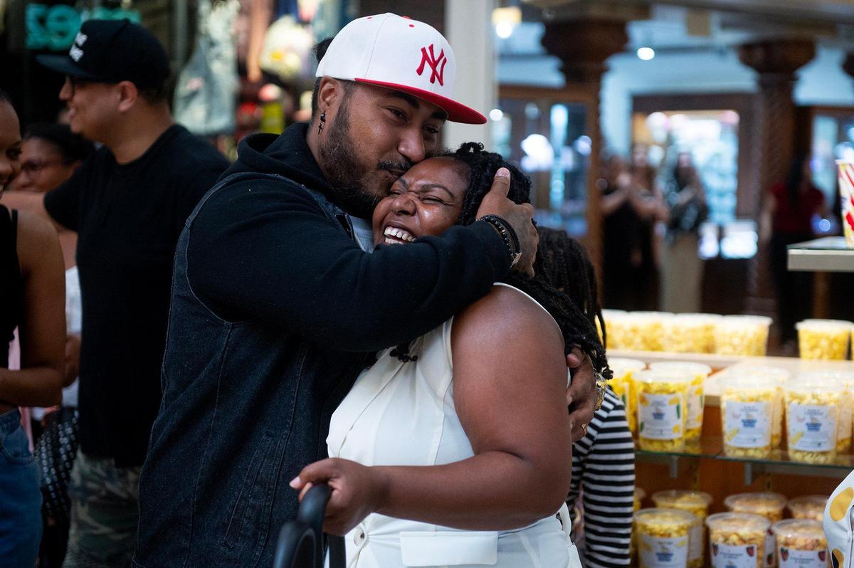 Dominique Pruitt, 36, of Merced, and owner of Dom’s Bomb Gourmet Popcorn, receives a kiss from husband Victor Perez, 39, during the grand opening of business’ kiosk at the Marketplace at Merced in Merced, Calif., on Thursday, May 1, 2025. The kiosk offers unique gourmet popcorn flavors created by Pruitt.
