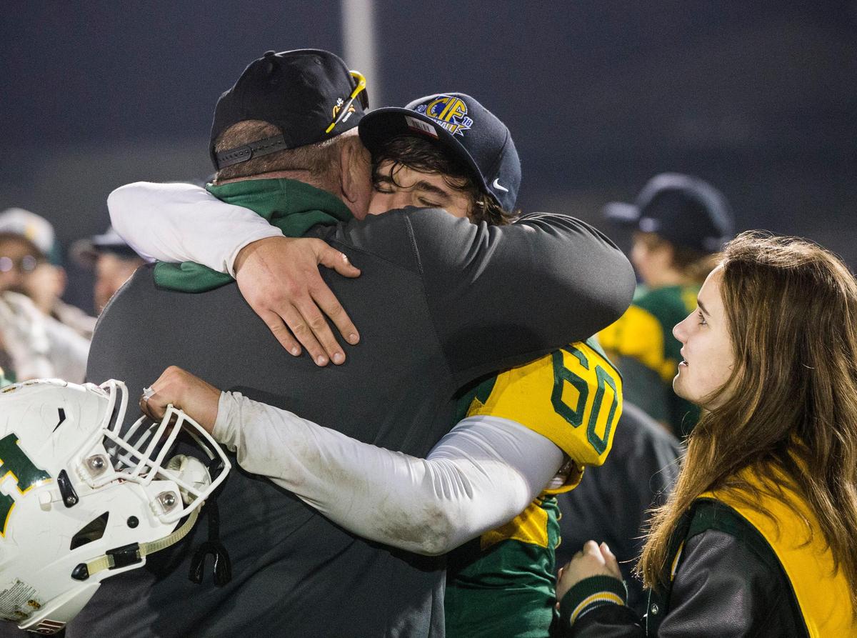 Brennan Mason, 60, of Hilmar High gets a hug from coach Brad Mason after winning the CIF State 6-AA High School Football State Championships against Strathmore High Saturday Dec. 15, 2018.