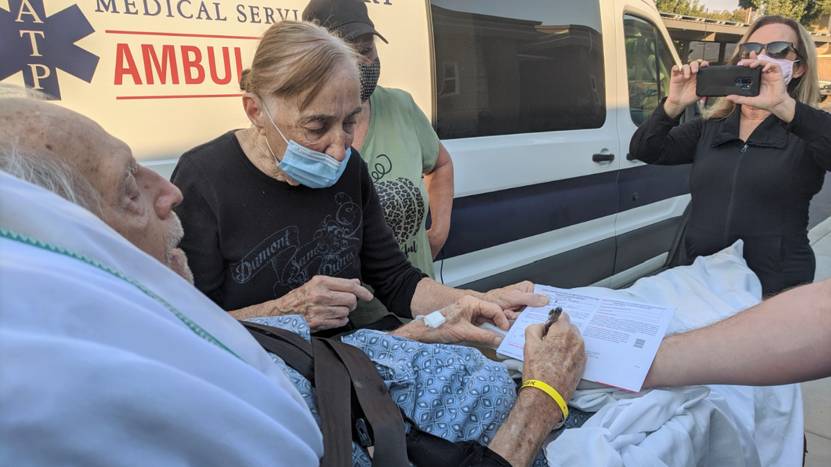 Merced resident Richard Howard, 89, signs his mail-in voting ballot while strapped to a gurney outside an ambulance on Thursday, Octobert 29, 2020 as his wife Mary and family look on in Merced, Calif.