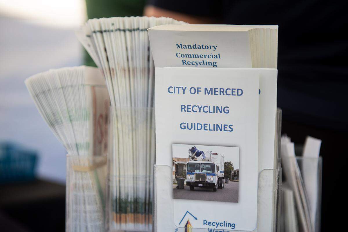 Various give away items with information about recycling sit on the table as City of Merced Recycling Coordinator Monique Gama, interacts with members of the community during the National Night Out event at Applegate Park in Merced, Calif., on Tuesday, Aug. 5, 2025. 