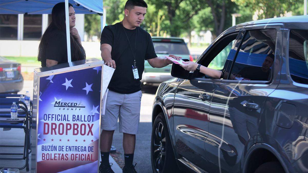 Election workers Alex Gonzales and Melina Gonzales help voters submit their ballots at the drive-through drop-off box in front of the Merced County Administration Building on Tuesday, June 7, 2022.