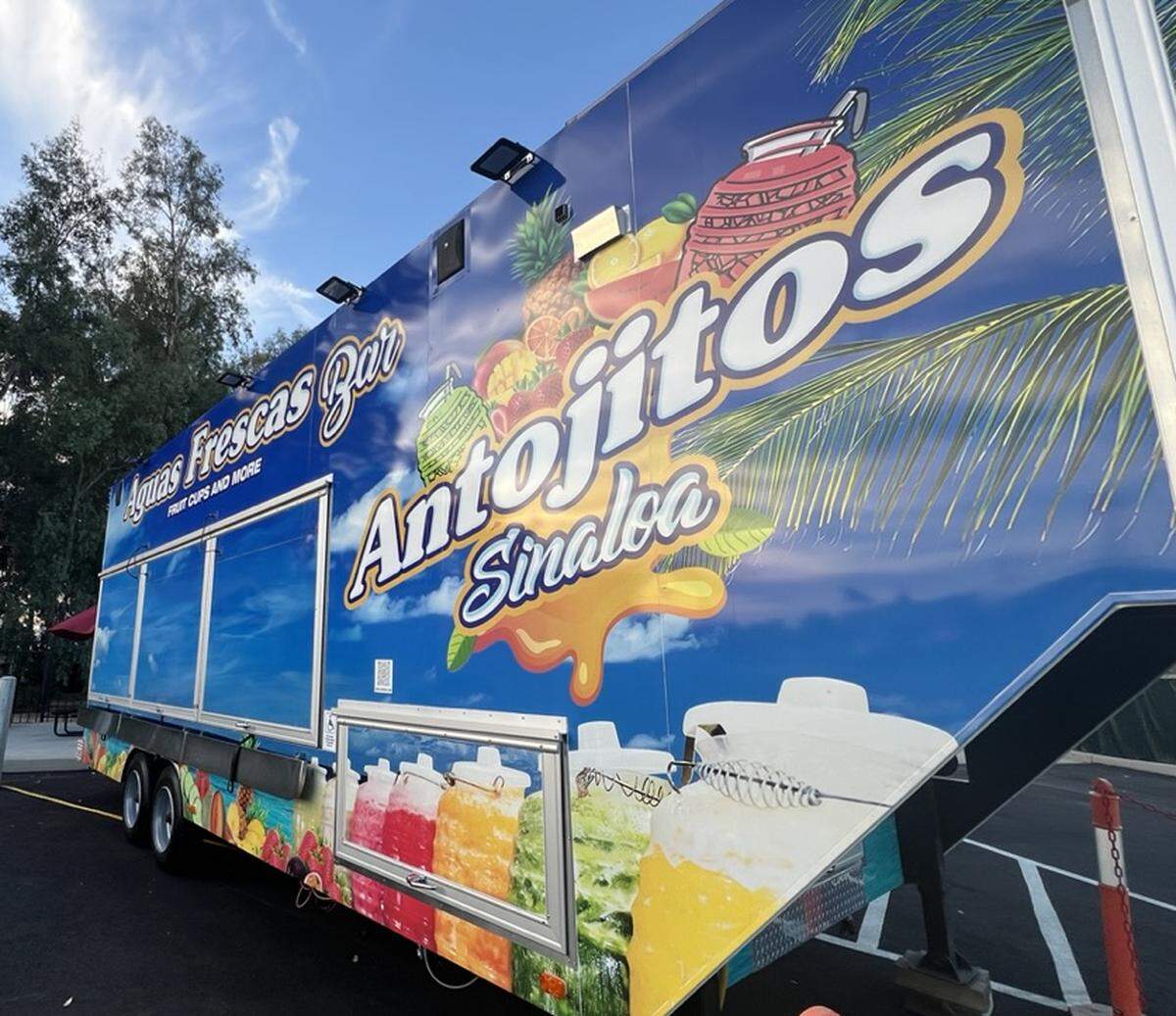 A closed food trailer with tropical fruit and agua frescas pictured on its sides. 