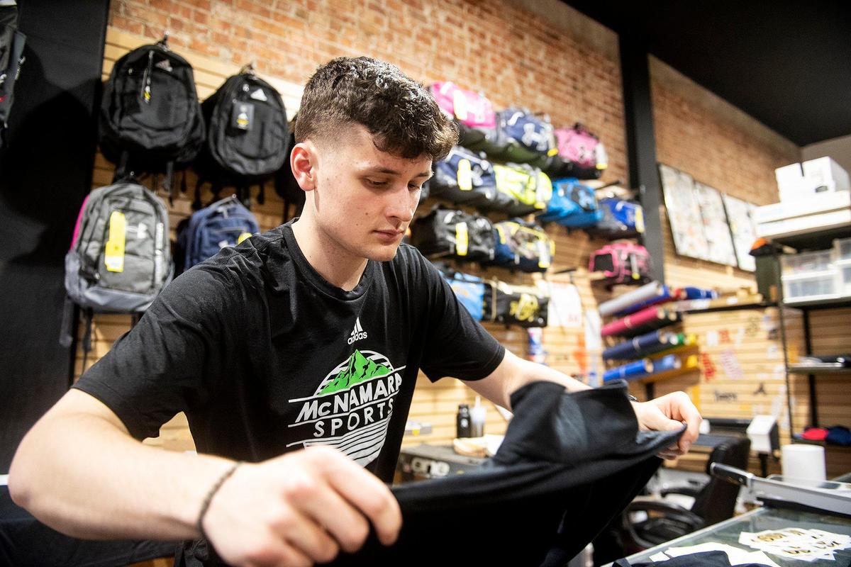 Jackson Kane, 20, of Merced, adds a logo to shirts at McNamara Sports, located at 437 W. 18th Street in Merced, Calif., on Monday, May 8, 2023. The family owned store which sells athletic equipment, team uniforms, business apparel and offers screen printing and embroidery services, is celebrating 100 years in business
