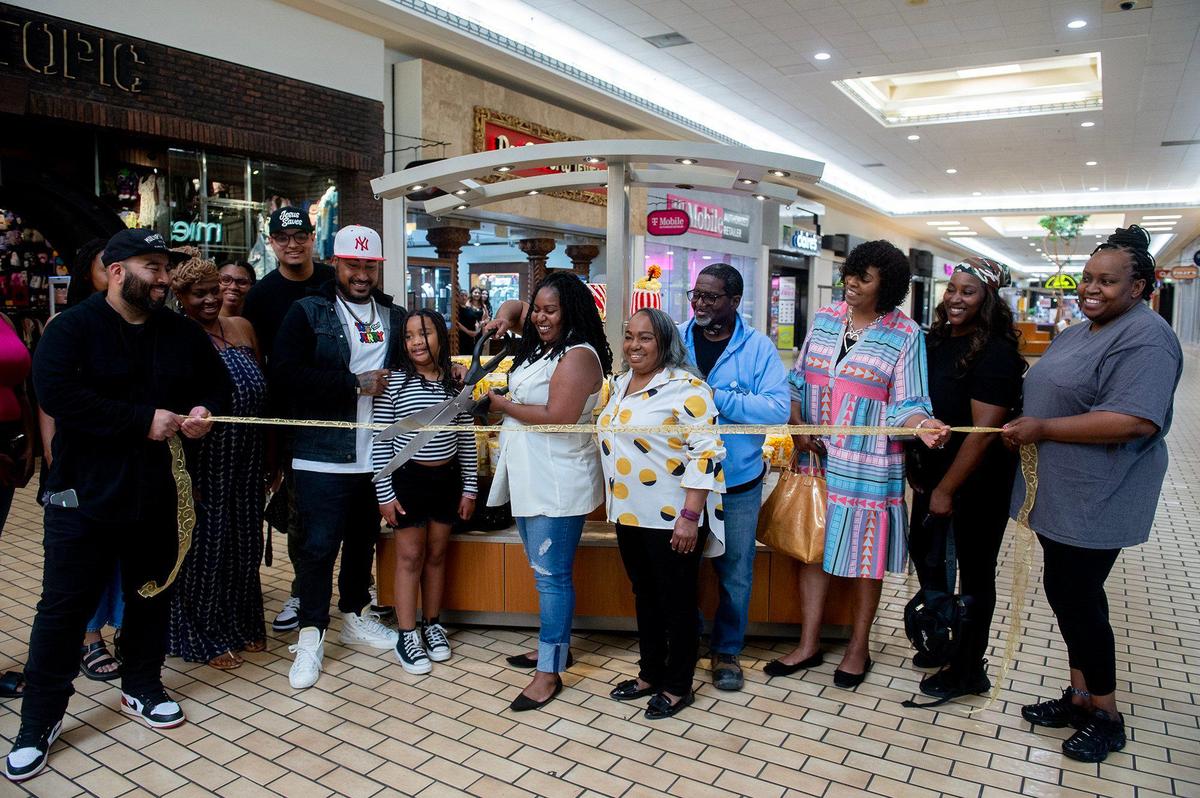 Dominique Pruitt, 36, of Merced, cuts the ribbon while surrounded by family and friends during the grand opening of Dom’s Bomb Gourmet Popcorn inside the Marketplace at Merced in Merced, Calif., on Thursday, May 1, 2025. The kiosk offers unique gourmet popcorn flavors created by Pruitt.